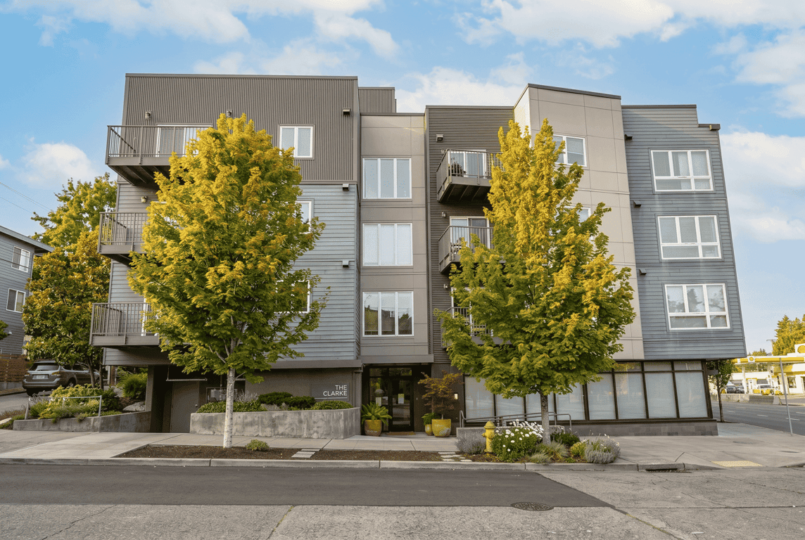 Modern apartment building exterior, The Clarke, with balconies, large windows, and trees under a ...